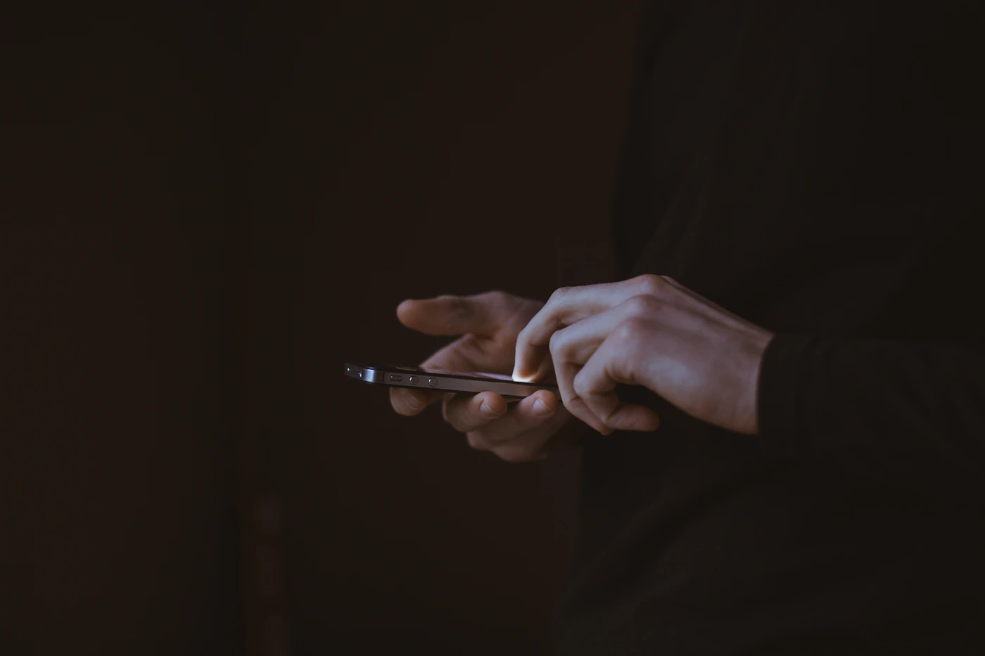 A silhouette holding a smartphone, the only light in the dark