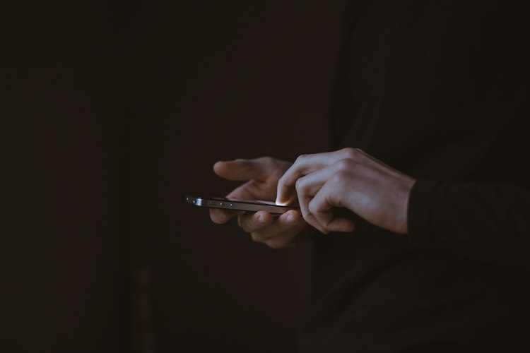 Person sitting alone on a couch at night, looking at a smartphone screen