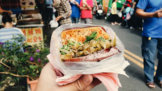A vibrant close-up of a hand holding a juicy NYC street food sandwich against an urban backdrop.
