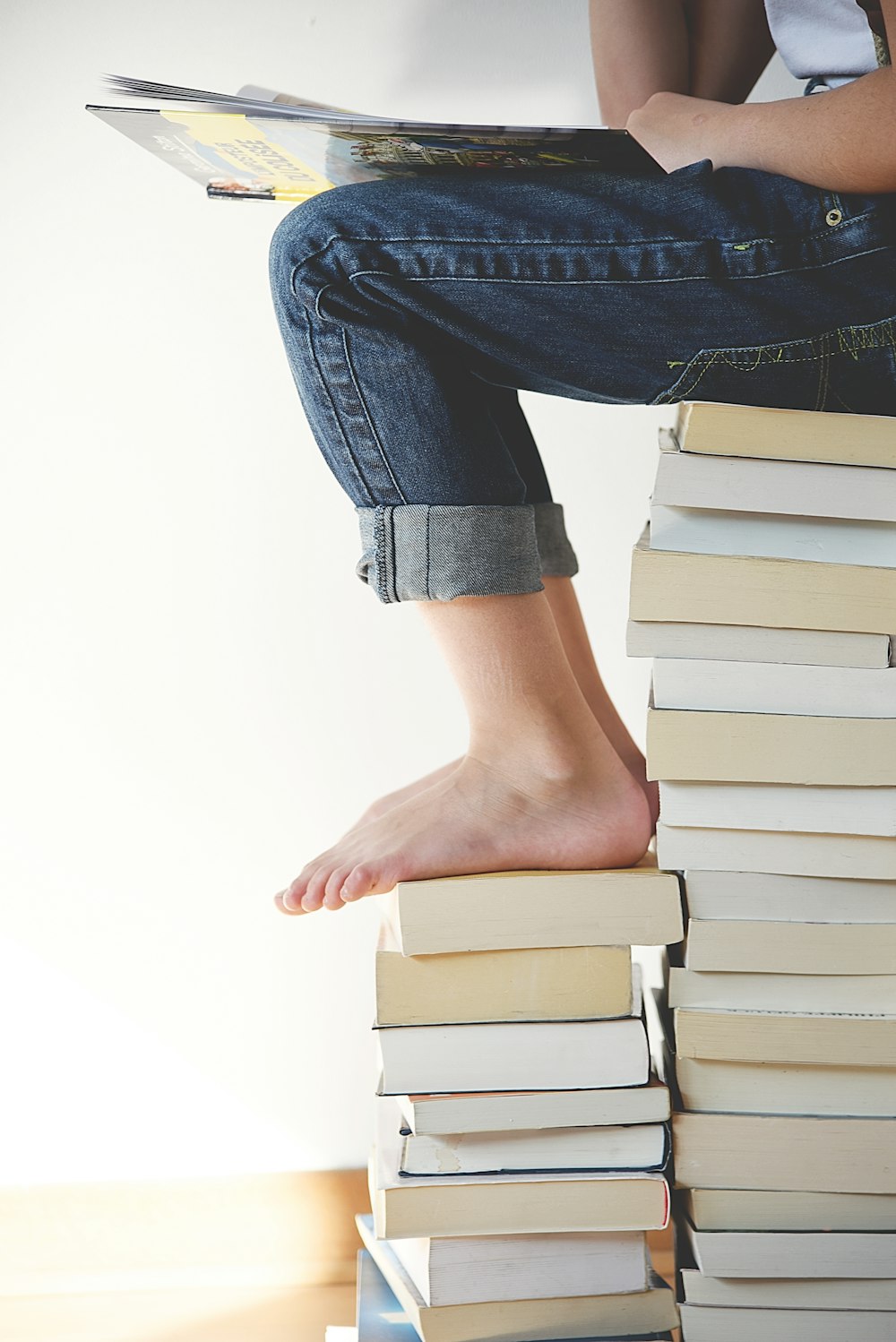 Person, die beim Lesen auf einem Bücherstapel sitzt