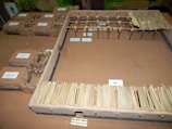 A miniature model showcasing a series of structures resembling traditional huts or enclosures, each labeled with Arabic text. The structures are enclosed by fences made of wooden sticks or similar materials. The layout seems to depict an organized settlement or village.