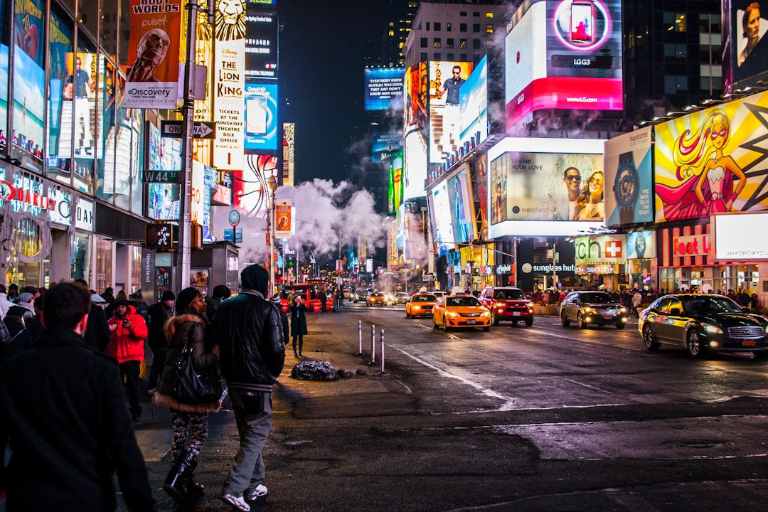 Pedestrians walk through the brightly lit Times Square at night while cars drive past