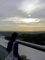 A traveler looking out over a bustling cityscape from a rooftop viewpoint at dusk.