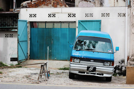 A sleek blue van parked by a suburban home, with a technician preparing detailing tools.