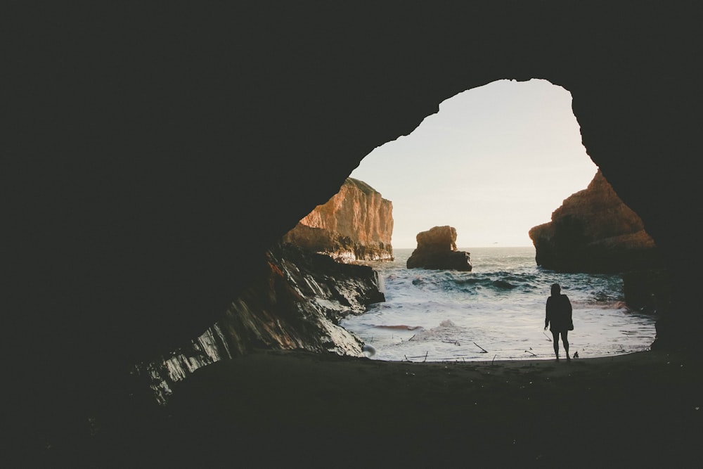 silhouette of person standing near body of water inside cave