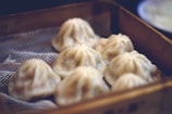 Several steamed dumplings are neatly arranged in a bamboo steamer basket. The dumplings have a smooth, pleated appearance with lightly translucent dough, suggesting freshness and warmth.
