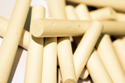 Several pieces of beige cylindrical chalk are scattered in a pile on a light surface, casting subtle shadows.
