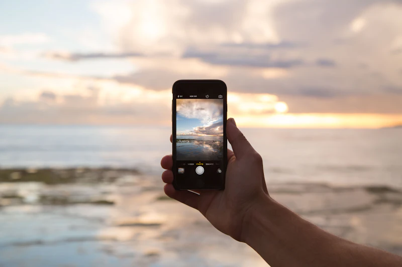 Hand holding a phone photographing the sea at sunset