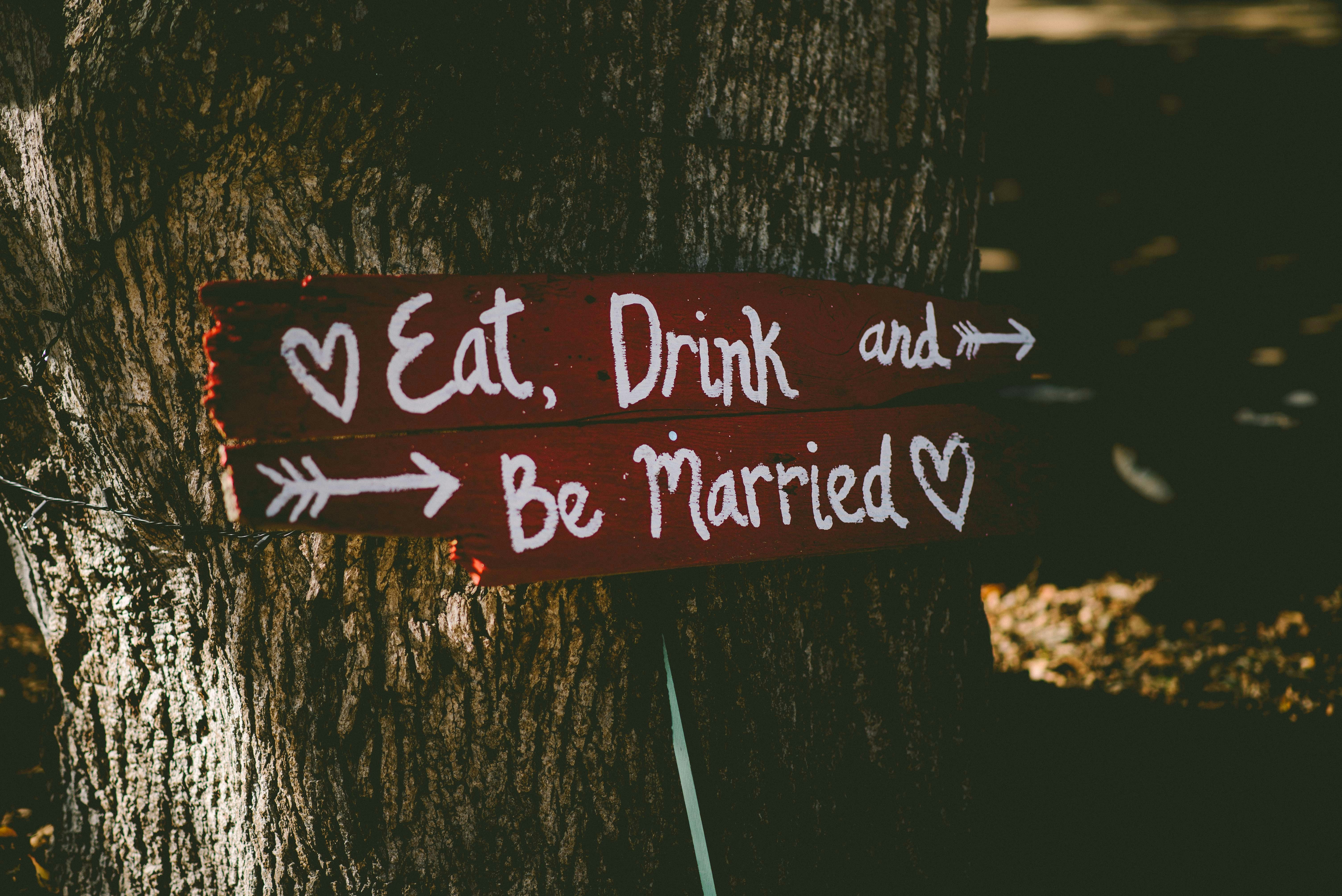 red and white eat, drink, and be married signage near brown tree