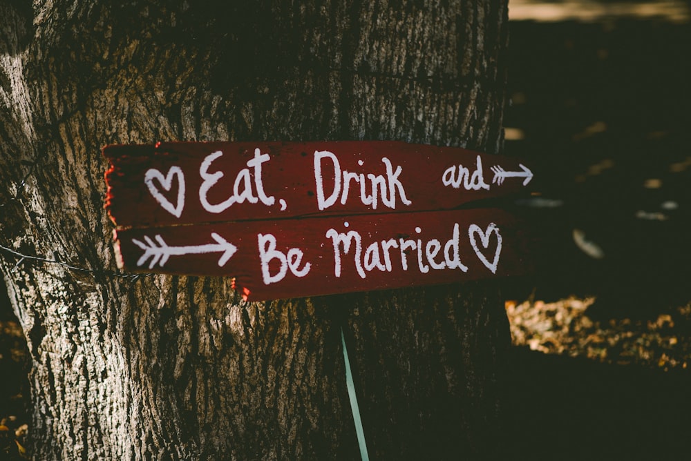 red and white eat, drink, and be married signage near brown tree