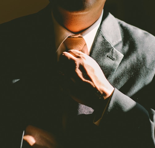 A man in a black suit loosening his tie