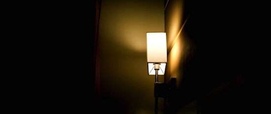 A soft, warm light emanates from a rectangular lamp mounted on a wall, casting gentle shadows and illuminating part of the dark room.