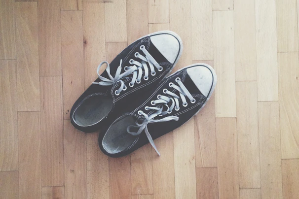 Close-up of classic black and white All Star sneakers on a wooden floor with soft natural light.