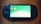 A handheld gaming console with a screen displaying icons and options for games and saved data. The device has typical gaming buttons and directional pads on either side of the screen.