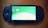 A handheld gaming console with a screen displaying icons and options for games and saved data. The device has typical gaming buttons and directional pads on either side of the screen.