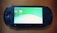 A handheld gaming console with a screen displaying icons and options for games and saved data. The device has typical gaming buttons and directional pads on either side of the screen.