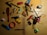 A collection of various household items scattered on a wooden surface. Items include a red comb, a compass, toy cars, a ruler, scissors, a folding ruler, a lighter, a stapler, a roll of tape, a stapler remover, and a highlighter. Most items are placed randomly in different orientations.