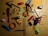 A collection of various household items scattered on a wooden surface. Items include a red comb, a compass, toy cars, a ruler, scissors, a folding ruler, a lighter, a stapler, a roll of tape, a stapler remover, and a highlighter. Most items are placed randomly in different orientations.