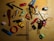 A collection of various household items scattered on a wooden surface. Items include a red comb, a compass, toy cars, a ruler, scissors, a folding ruler, a lighter, a stapler, a roll of tape, a stapler remover, and a highlighter. Most items are placed randomly in different orientations.