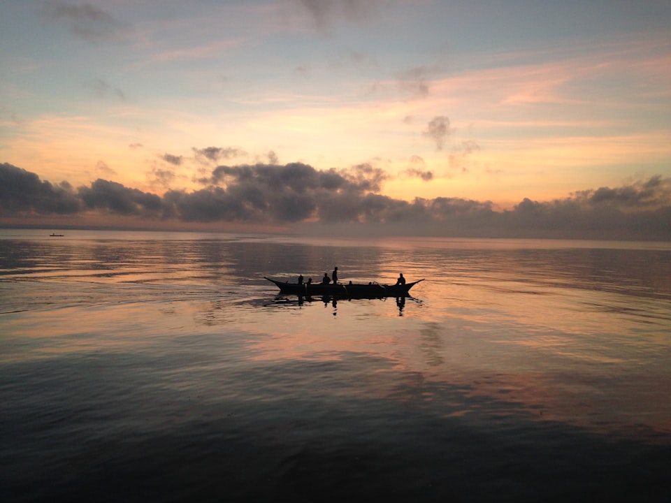 A fishing boat on calm waters silhouetted against a cloudy sunset