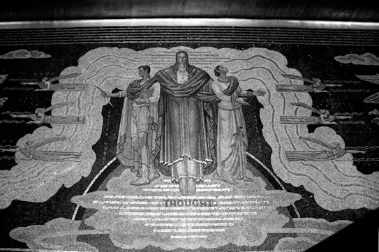 A detailed mural depicting three central human figures dressed in draped garments, possibly indicating classical or historical influences. The central figure raises an arm, and they are flanked by two others who are gesturing outward. Surrounding them are clouds and what appears to be winged human forms or mythical creatures. The word 'THOUGHT' is prominently displayed beneath the central figure's feet.