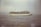 A large cruise ship sails on the calm sea, with a slight haze in the sky and a distant coastline visible on the left. The ship is detailed with multiple decks, and lifeboats are visible on the side.