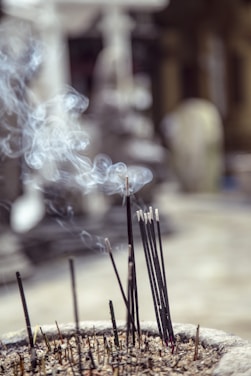 Close-up of a hand holding a bundle of glowing, triple-scented incense sticks against a soft, warm background.