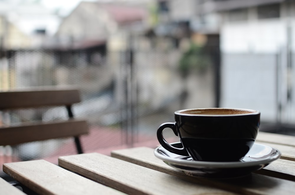 selective focus photography of black ceramic tea mug and plate on brown wooden table during daytime