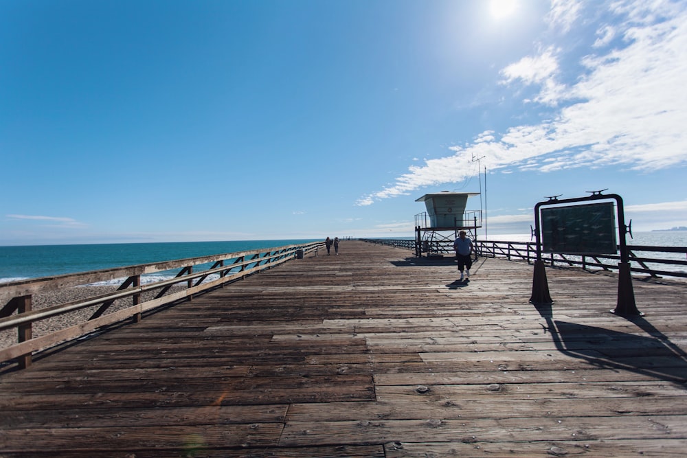 people on brown wooden pathway under blue sky