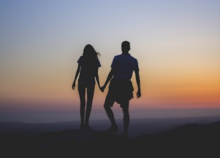 man and woman holding hands in silhouette photography