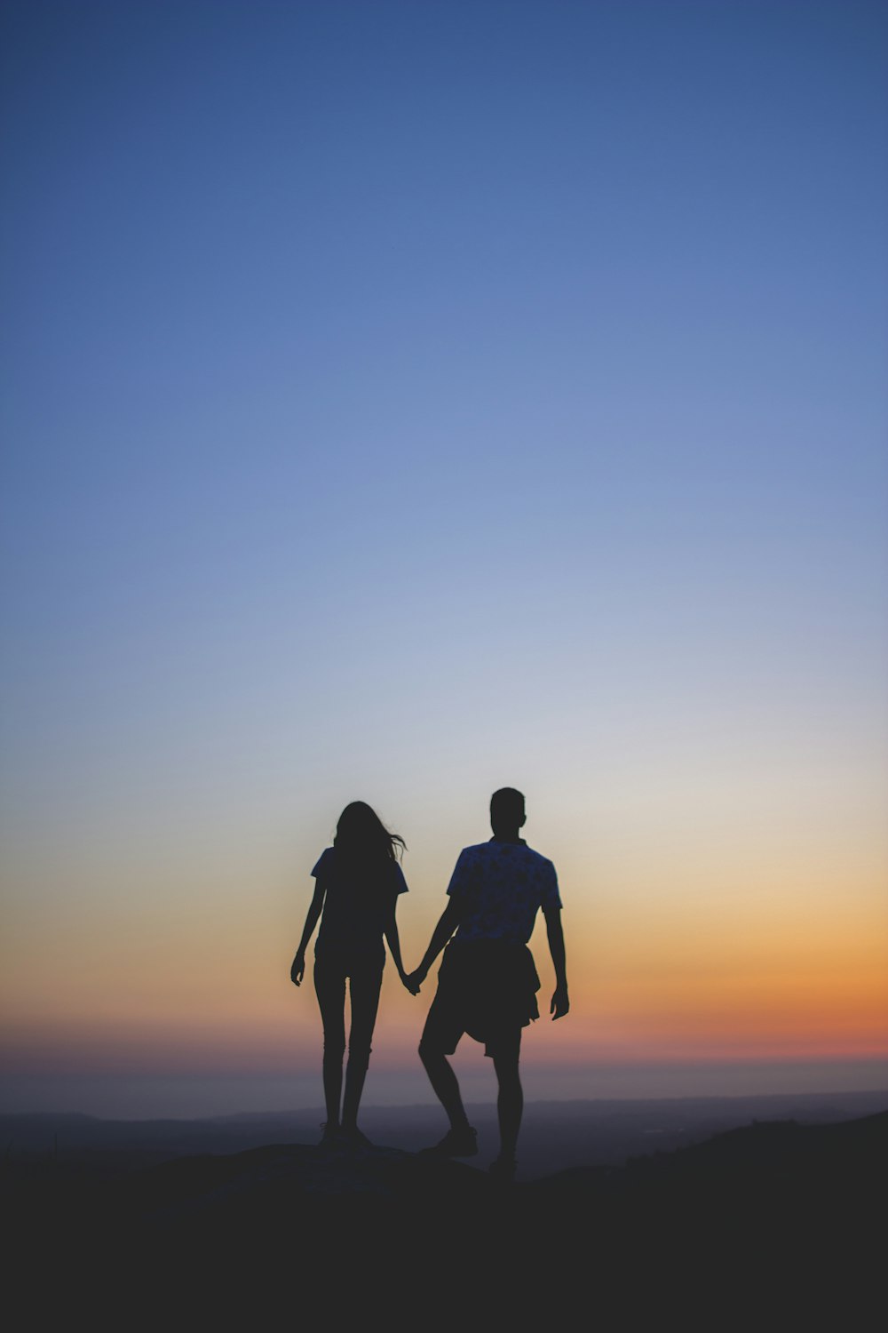 man and woman holding hands in silhouette photography