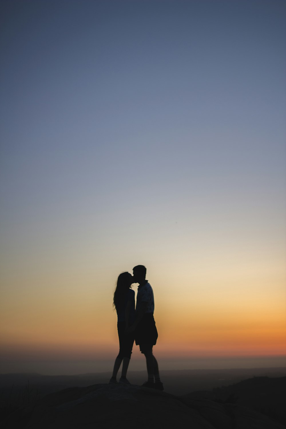 Two people kiss silhouetted against a sunset sky