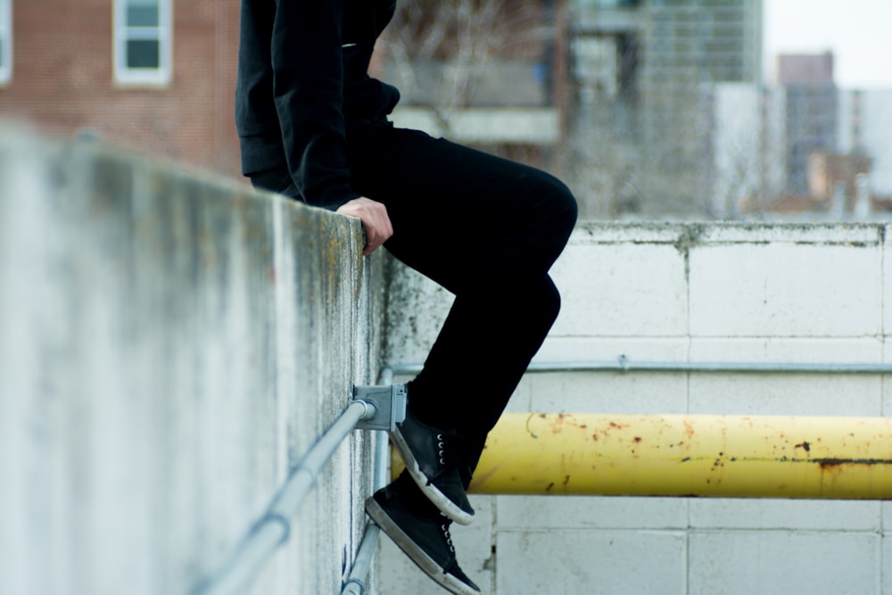 person sitting on top of white concrete wall near yellow metal pipe