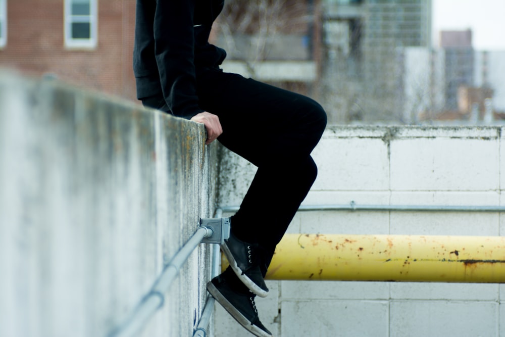 pessoa sentada em cima da parede de concreto branco perto do tubo de metal amarelo