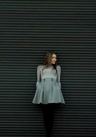 A sophisticated woman wearing dark blue jeans and a cream blouse posed against a deep navy wall with subtle golden accents.
