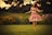 A model twirling in a vibrant, long dress in a sunlit outdoor garden.