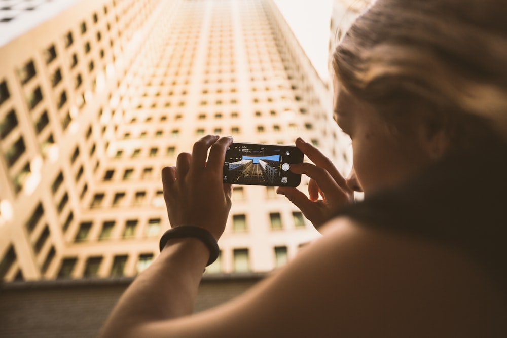 selective focus photography of woman taking low angle photo of high-rise building