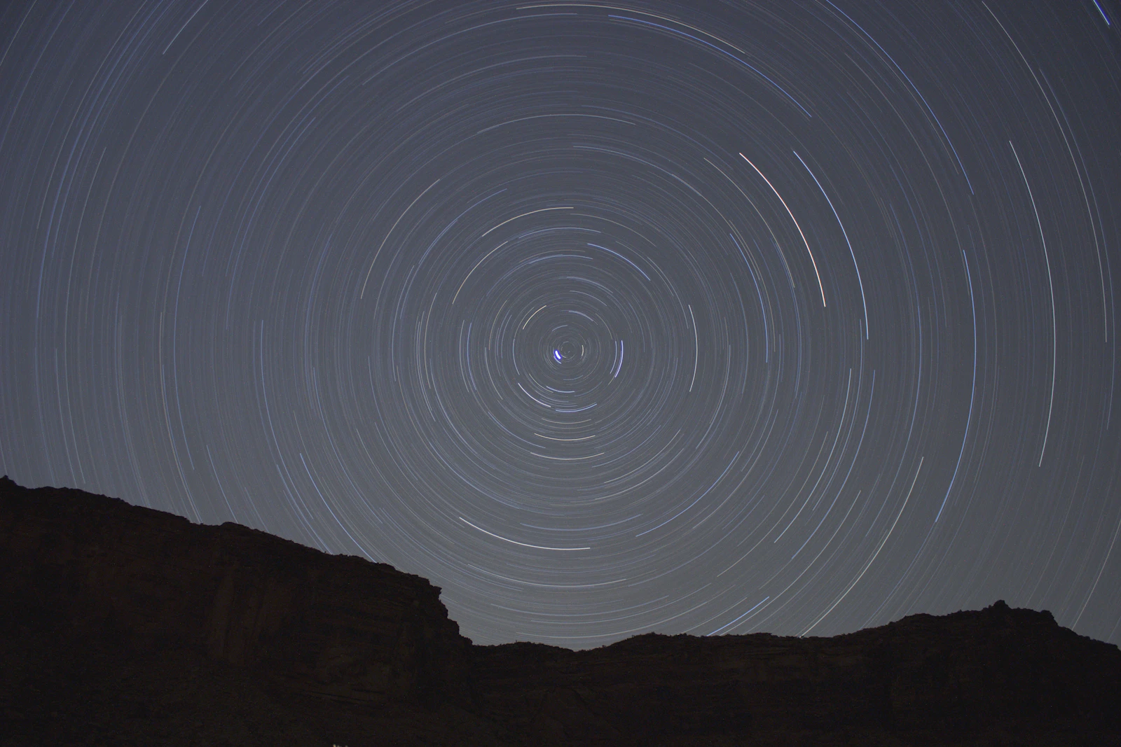 Concentric star trails circling over a silhouetted rock face at night