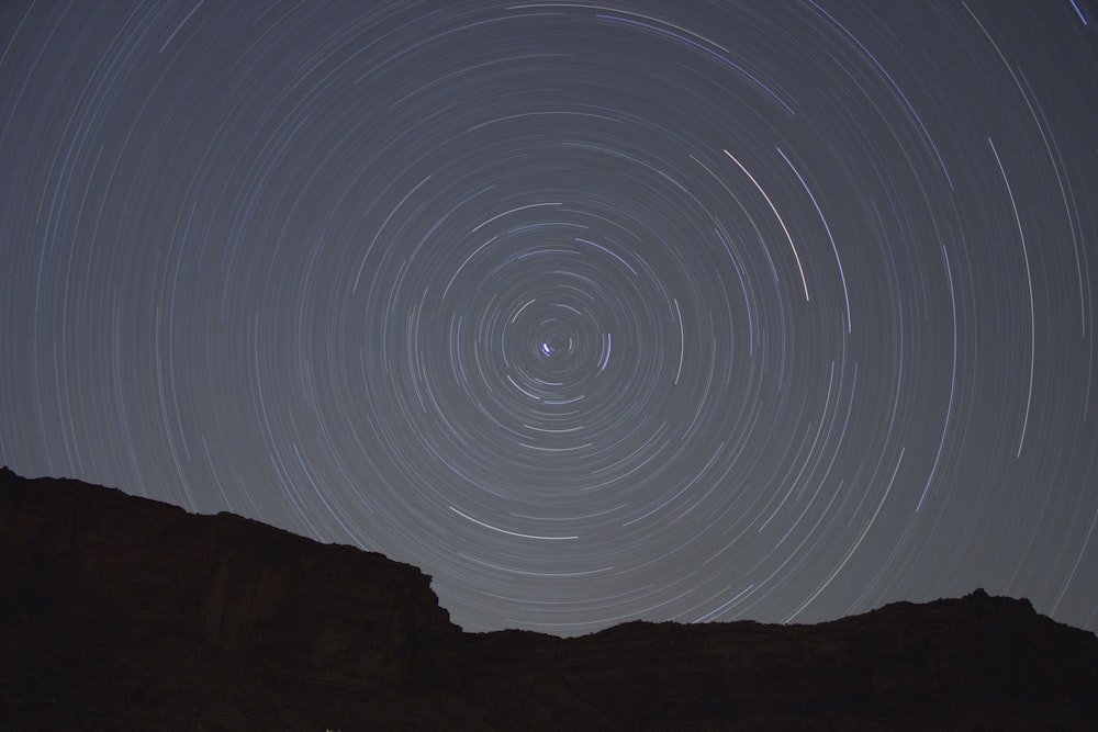 Concentric circles created by stars moving through the night sky over a silhouetted rock face