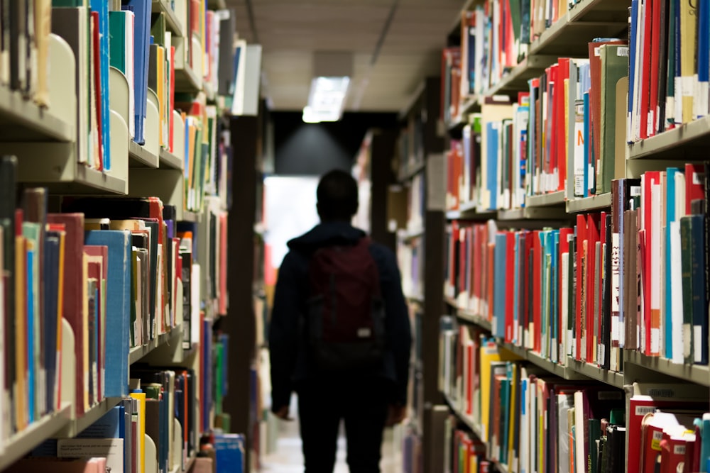 man with backpack beside a books