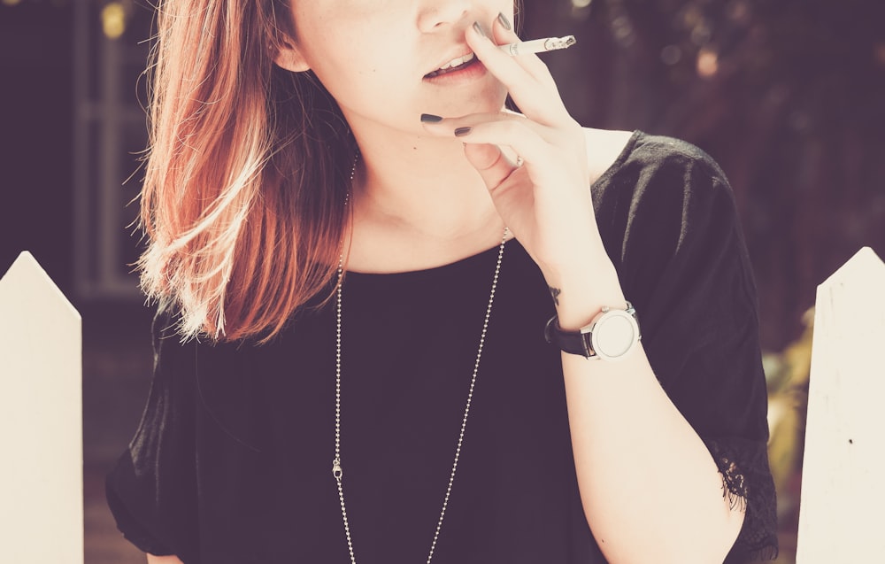 woman smoking beside white fence