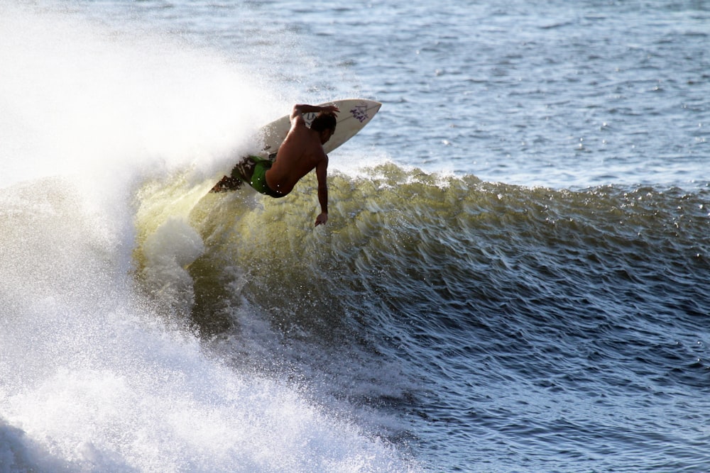 Mann surft mit weißem Holz-Surfbrett auf dem Meer