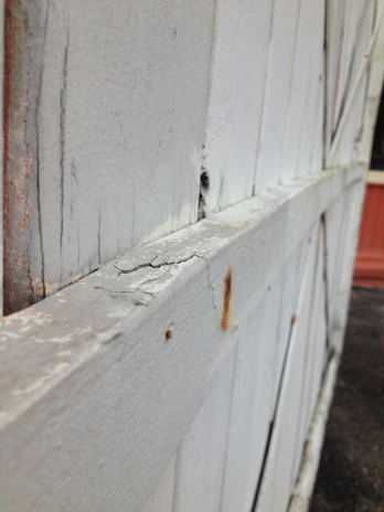 A close-up of a weathered wooden fence half cleaned, showing a stark contrast between dirt and fresh wood.