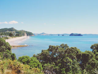A scenic view of Lombok's pristine beach with clear blue waters and lush green hills in the background.