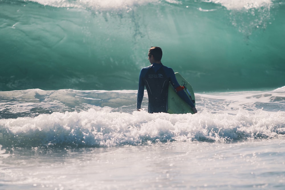 homem em pé no corpo de água segurando prancha de surf