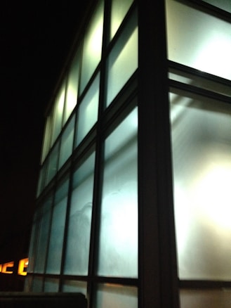 The image features a building with a modern architectural design, characterized by large frosted glass panels arranged in a grid. The luminous glow from within the building creates a calming ambiance against the night sky.