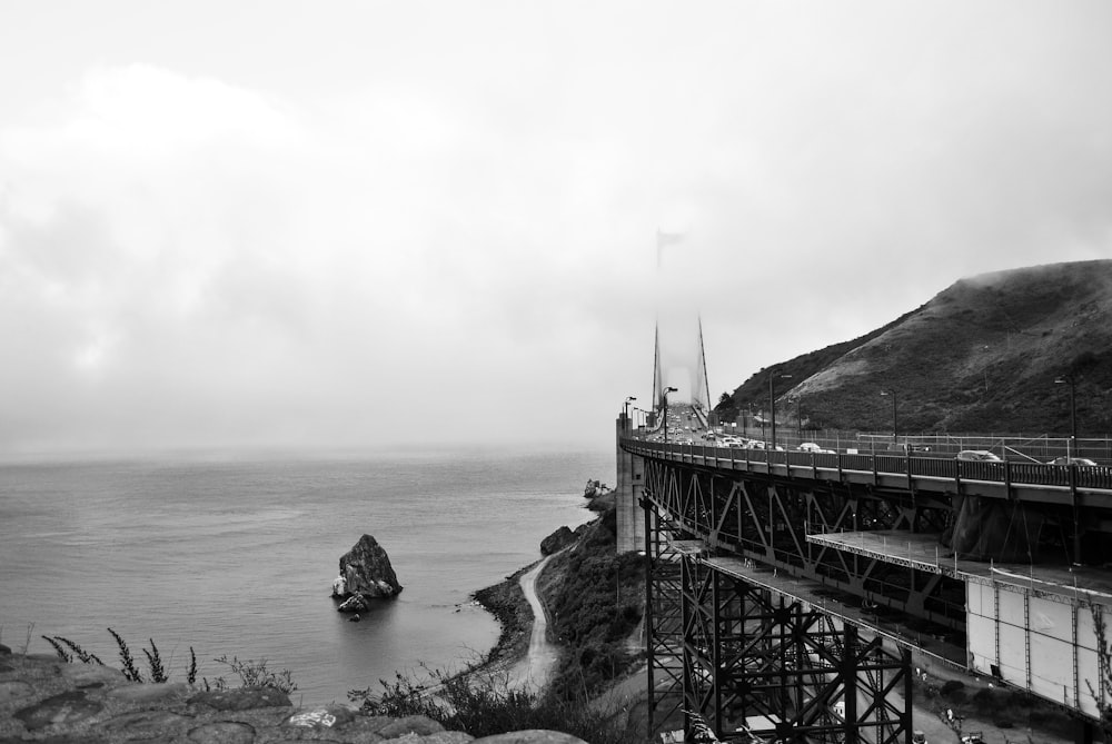 gray scale photo of bridge near body of water