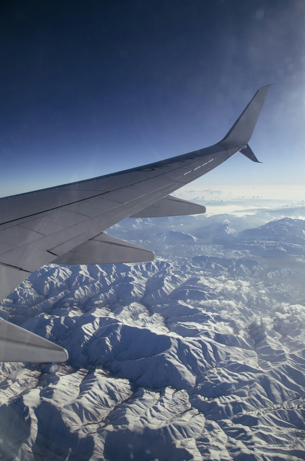 白と黒の飛行機の翼 昼間、白と青の山々の上空を飛ぶ