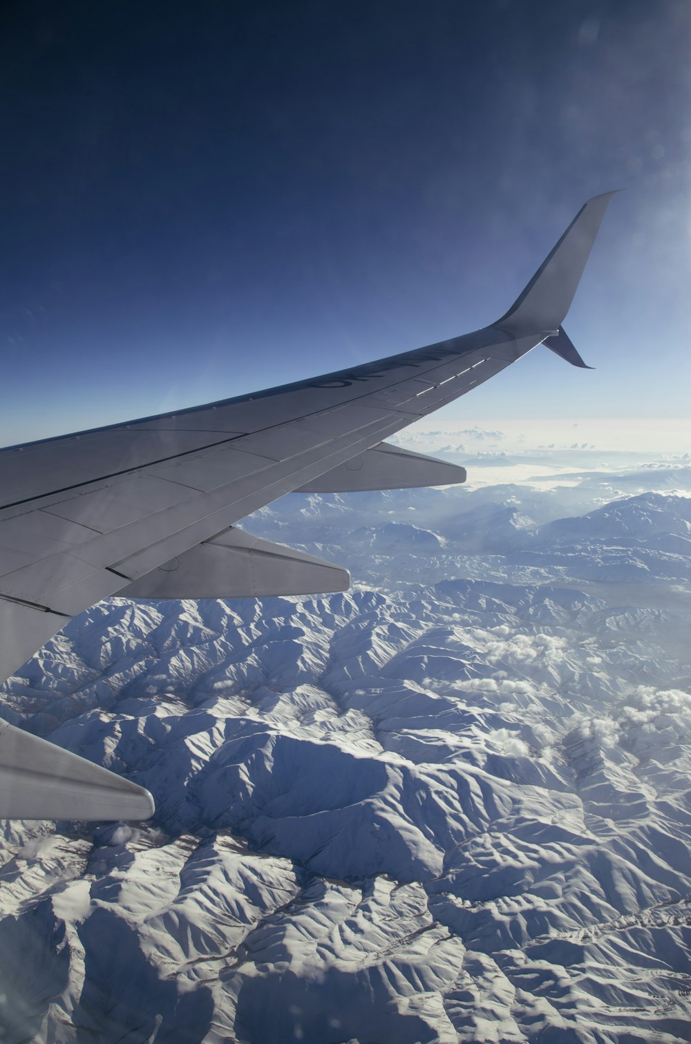 Ala de avión blanca y negra sobre montañas blancas y azules durante el día