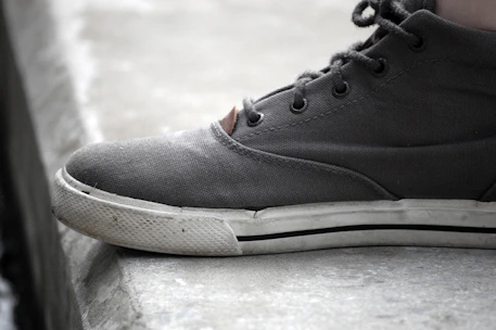 Close-up of a worn basketball sneaker resting on a gritty gym floor with subtle burnt orange laces.